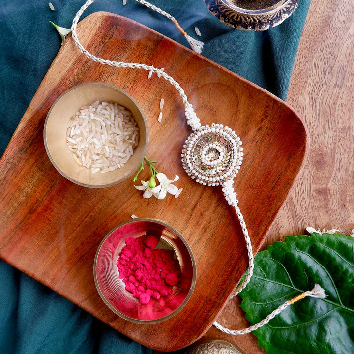 Handmade Zardozi White And Golden Rakhi With Wooden Box And Roli Chawal - Front View on Wooden Plate