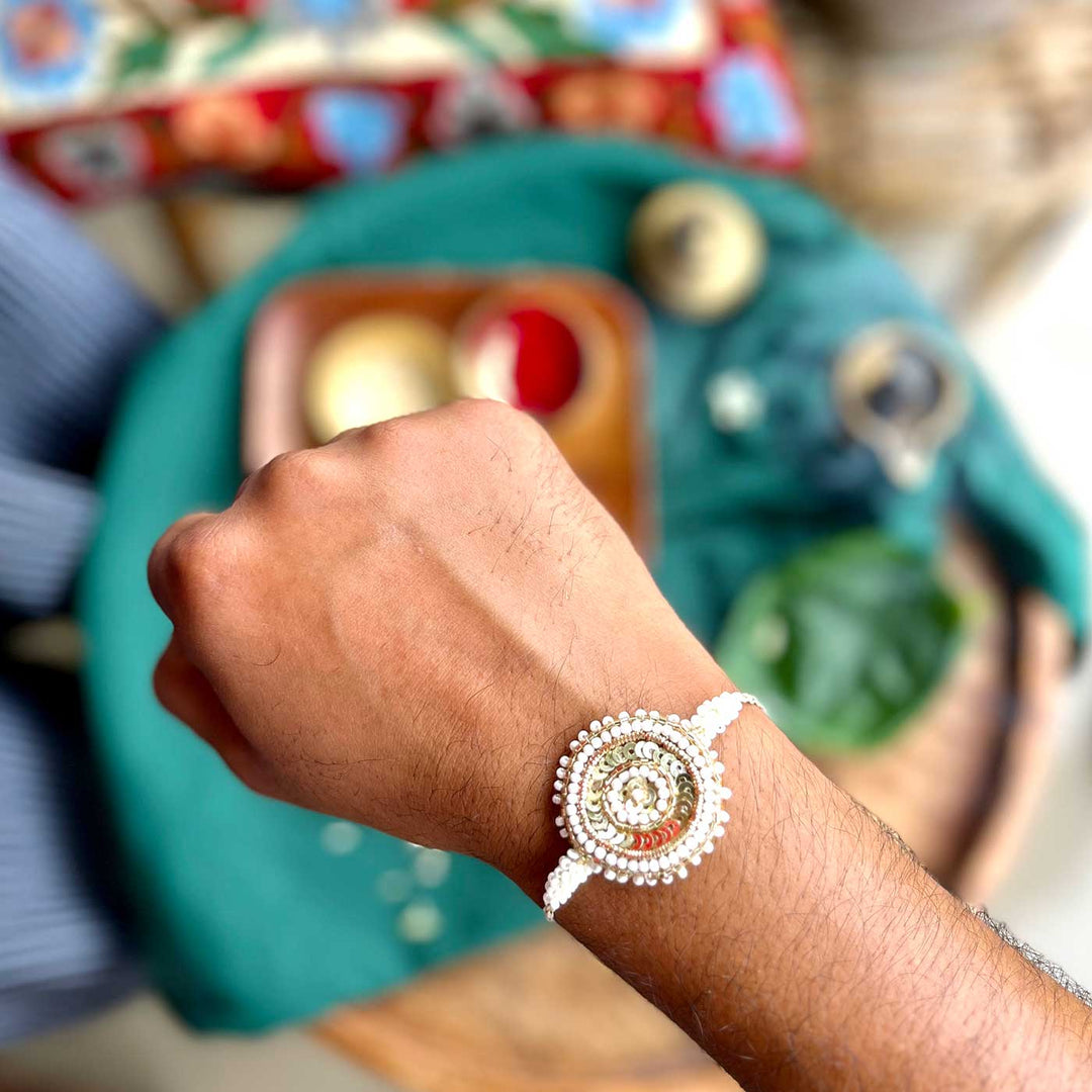 Handmade Zardozi White And Golden Rakhi With Wooden Box And Roli Chawal - Worn on Wrist Close-up