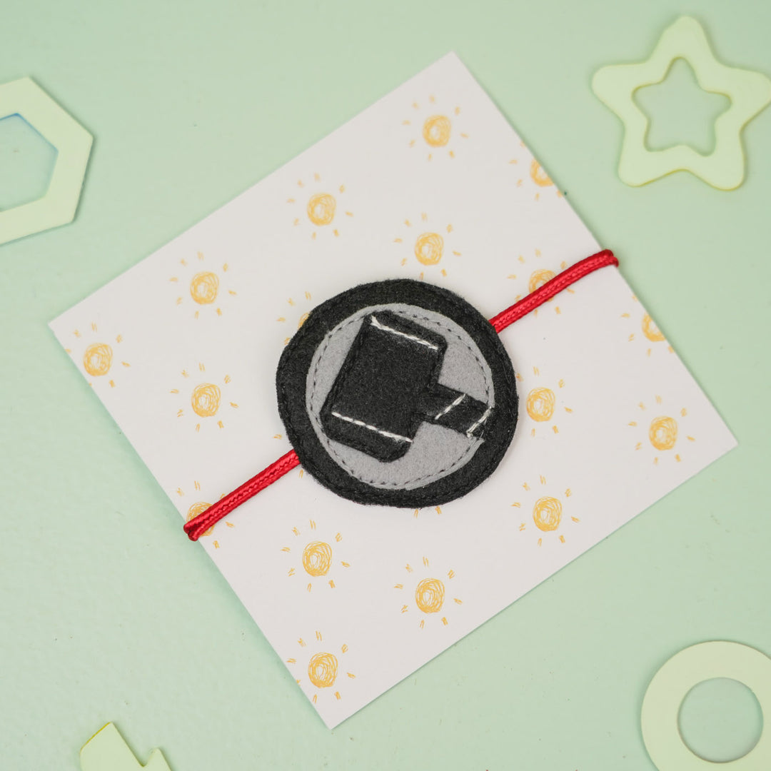 Handmade Thor Hammer Theme Felt Kids Rakhi For Brother - Tilted View on Patterned Card