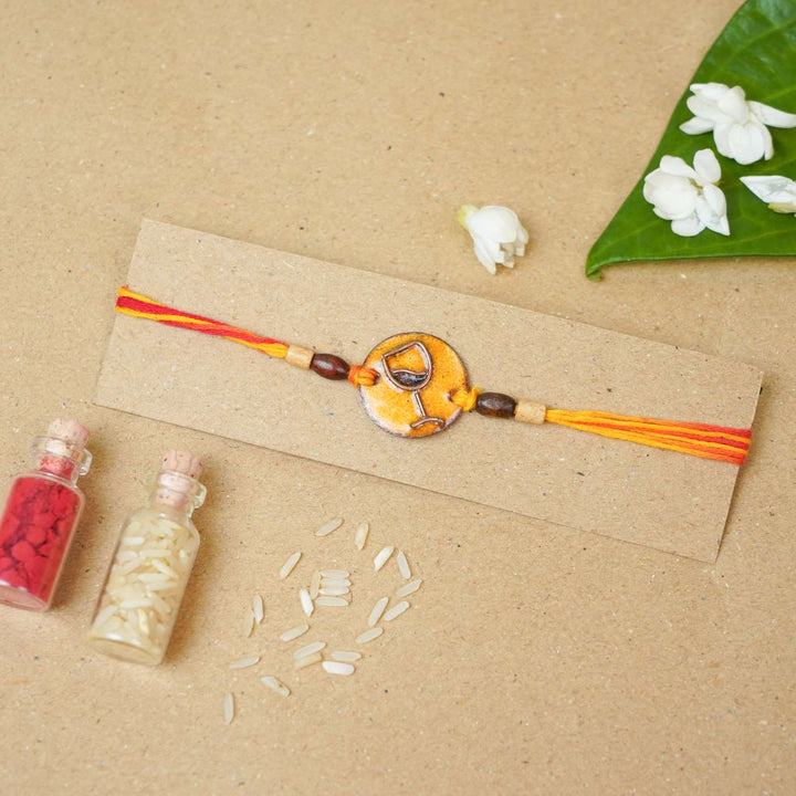 Handmade Wine O Clock Copper Enamel Rakhi With Chocolates And Roli Chawal - Bracelet displayed on packaging card