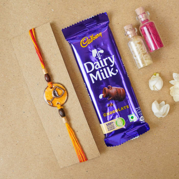 Handmade Wine O Clock Copper Enamel Rakhi With Chocolates And Roli Chawal - Product with gift items arrangement