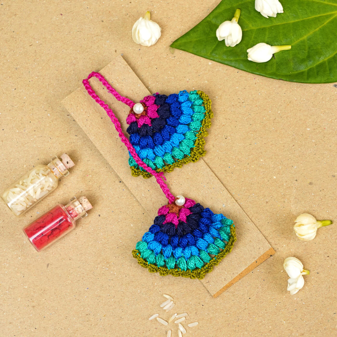 Handmade Crochet Peacock Cotton Lumba Rakhi For Bhabhi With Roli Chawal - Styled flat lay with decorations