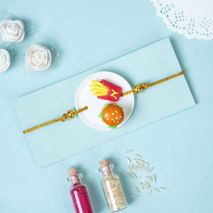 Handmade Miniature Clay Burger And Fries Rakhi With Roli Chawal - Rakhi on Blue Envelope Background