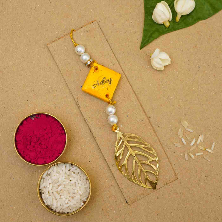 Personalized Handmade Yello Resin Lumba Rakhi For Bhabhi With Roli Chawal - Flatlay with personalized rakhi and ingredients