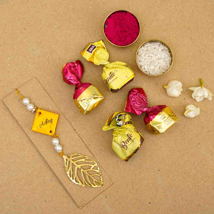 Personalized Handmade Yello Resin Lumba Rakhi For Bhabhi With Roli Chawal - Flatlay personalized rakhi with chocolates