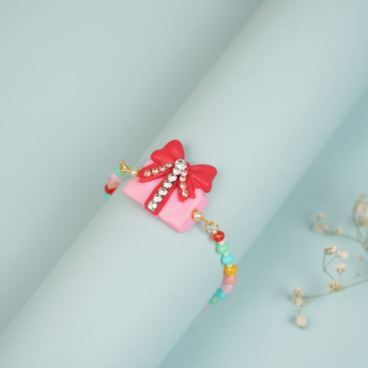 Handmade Beaded Gift Box Theme Clay Bracelet Rakhi With Roli Chawal For Sisters - Side View on Cylindrical Holder