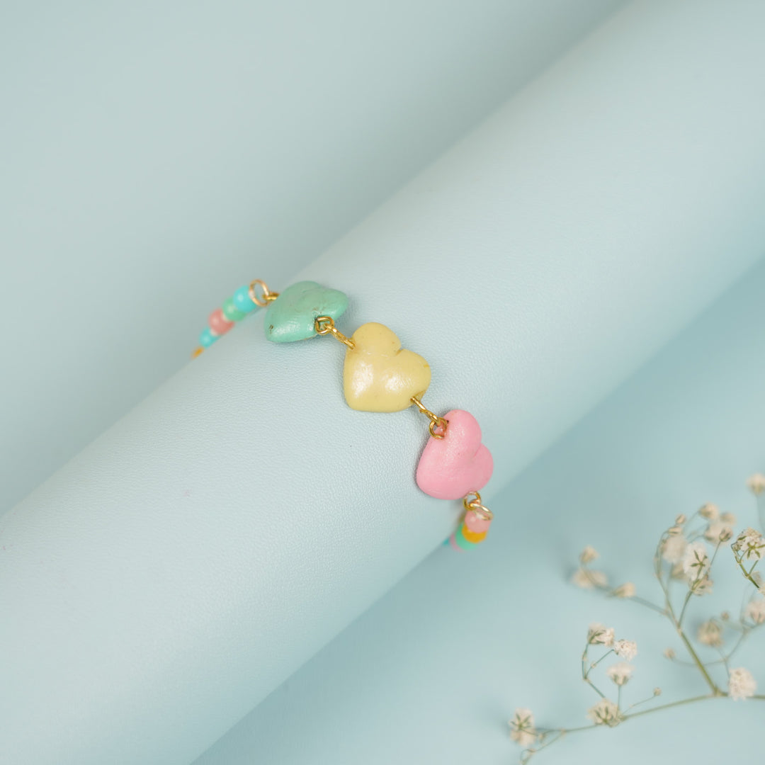 Handmade Beaded Multicolour Hearts Clay Bracelet Rakhi With Roli Chawal For Sisters - Bracelet wrapped on display tube