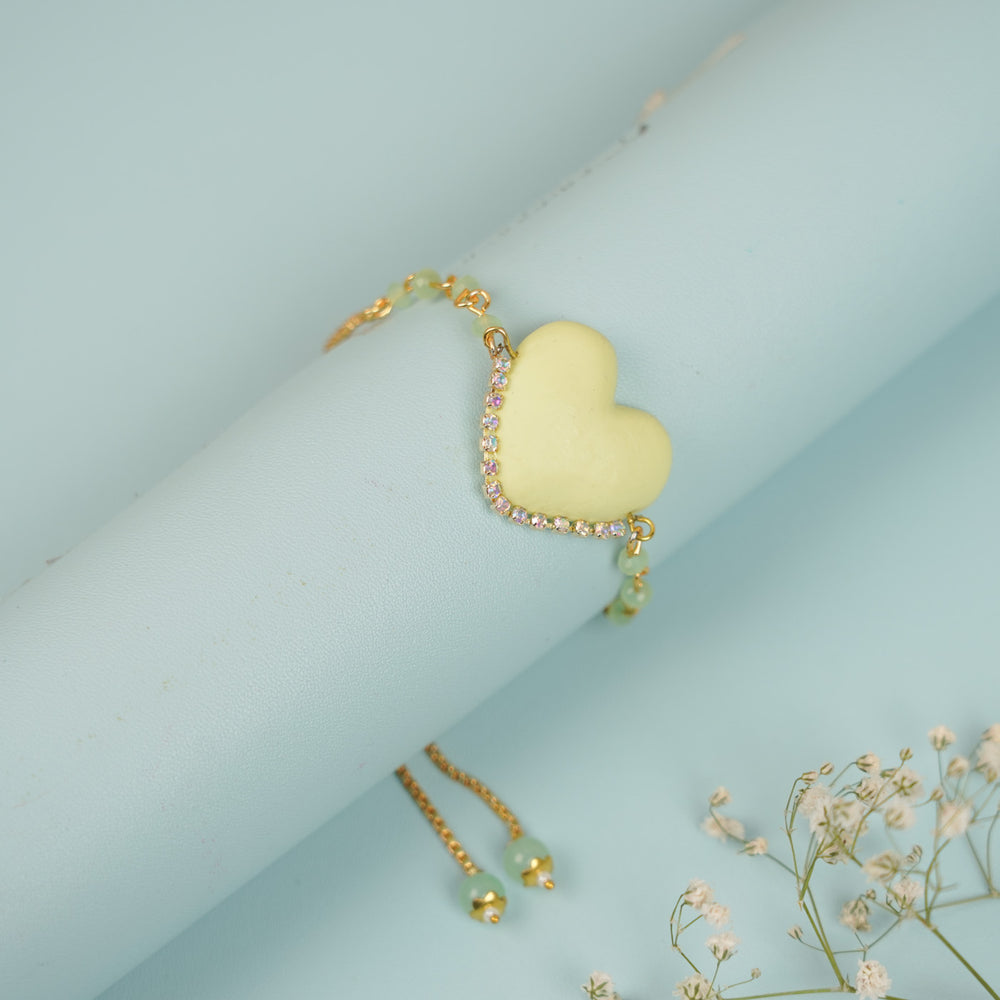 Handmade Beaded Yellow Heart Shaped Clay Bracelet Rakhi With Roli Chawal For Sisters - Bracelet Displayed on Wrist Prop