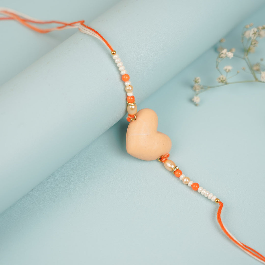 Handmade Beaded Orange Heart Shaped Clay Rakhi With Roli Chawal - Side view showing beige heart detail