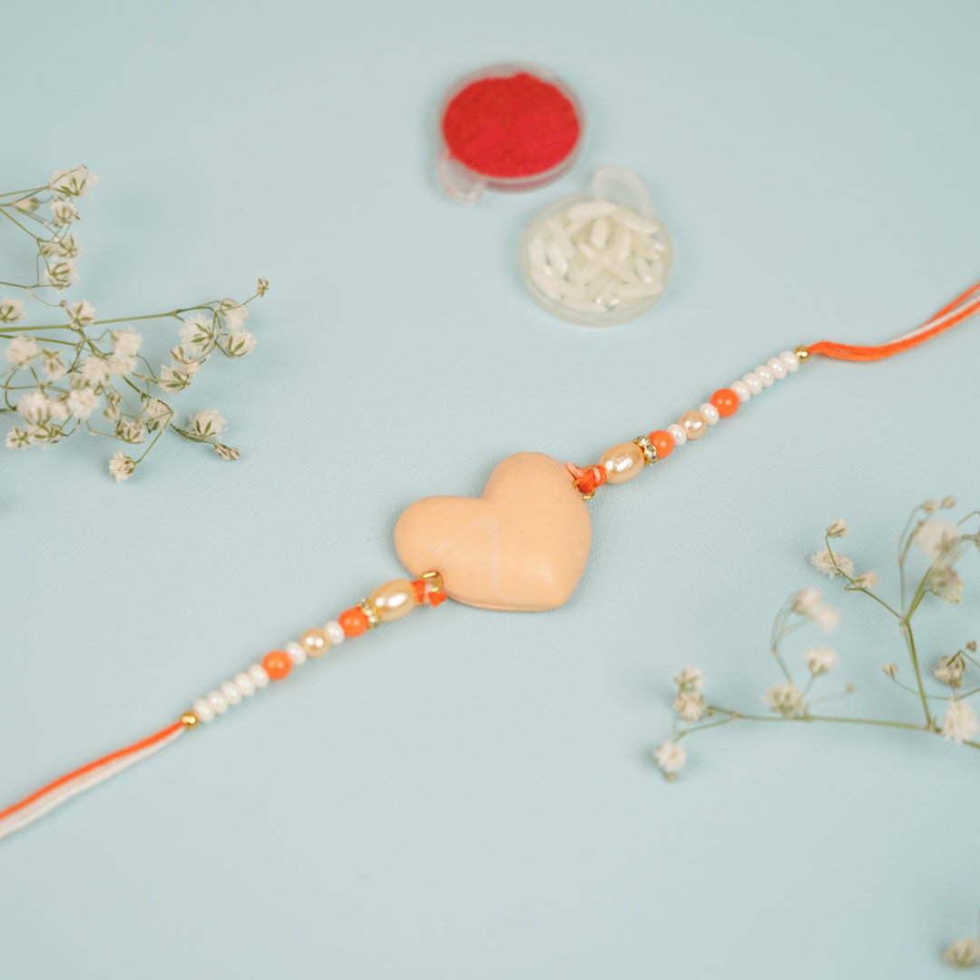 Handmade Beaded Orange Heart Shaped Clay Rakhi With Roli Chawal - Close-up of beige heart rakhi