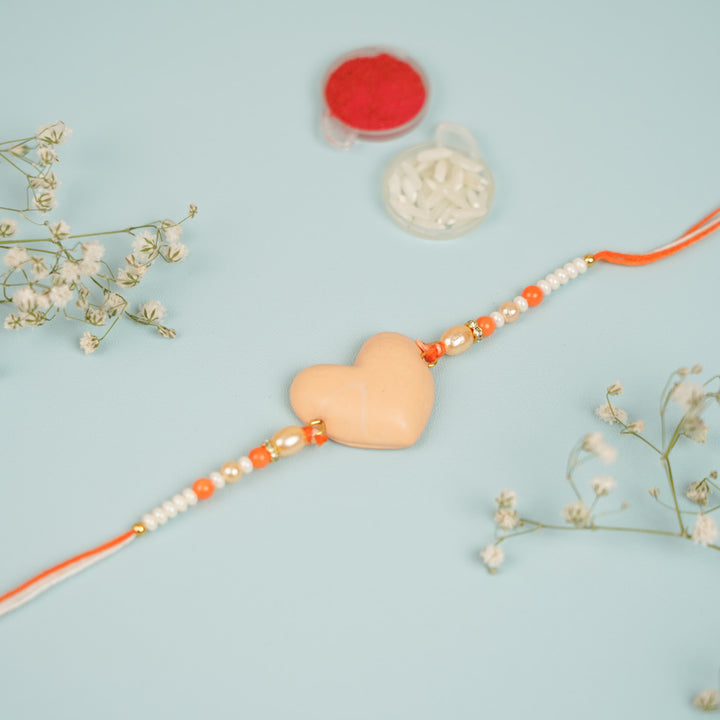 Handmade Beaded Orange Heart Shaped Clay Rakhi With Roli Chawal - Close-up of beige heart rakhi