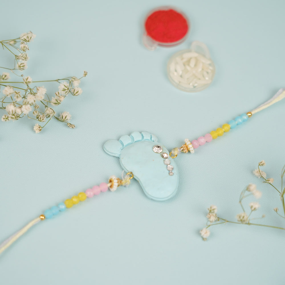 Handmade Blue And Pink Baby Feet Clay Bhaiya Bhabhi Rakhi With Roli Chawal Set Of 2 - Flat Lay with Accessories