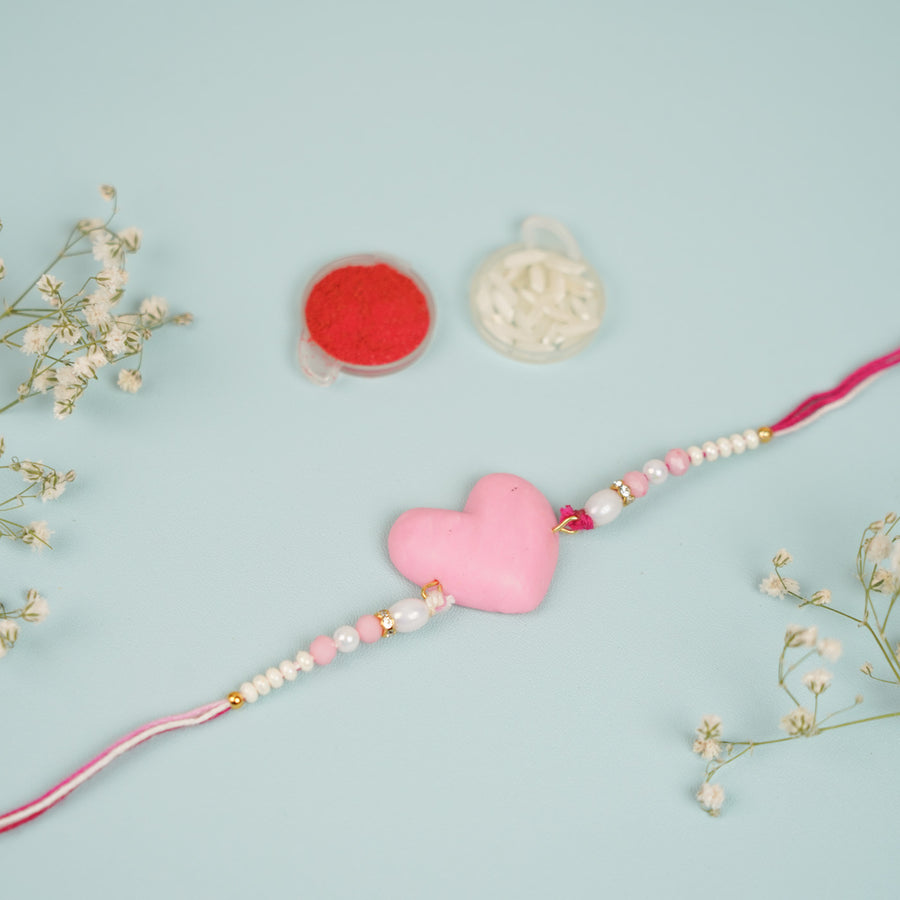 Handmade Beaded Pink Heart Shaped Clay Rakhi With Roli Chawal For Sisters - Close-up with Accessories