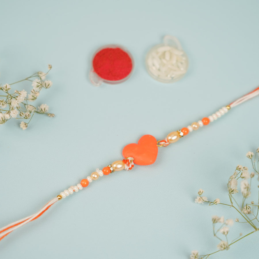 Handmade Beaded Orange Heart Shaped Clay Rakhi With Roli Chawal - Close-up of orange heart rakhi