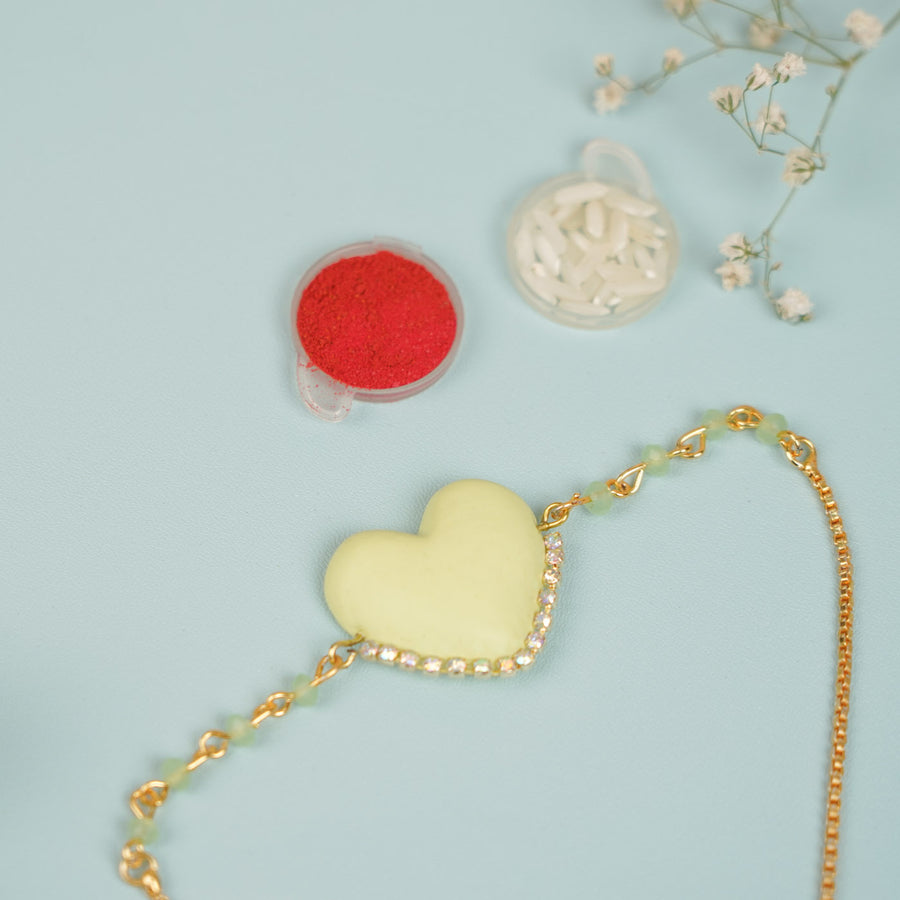 Handmade Beaded Yellow Heart Shaped Clay Bracelet Rakhi With Roli Chawal For Sisters - Close-up with decorative powders