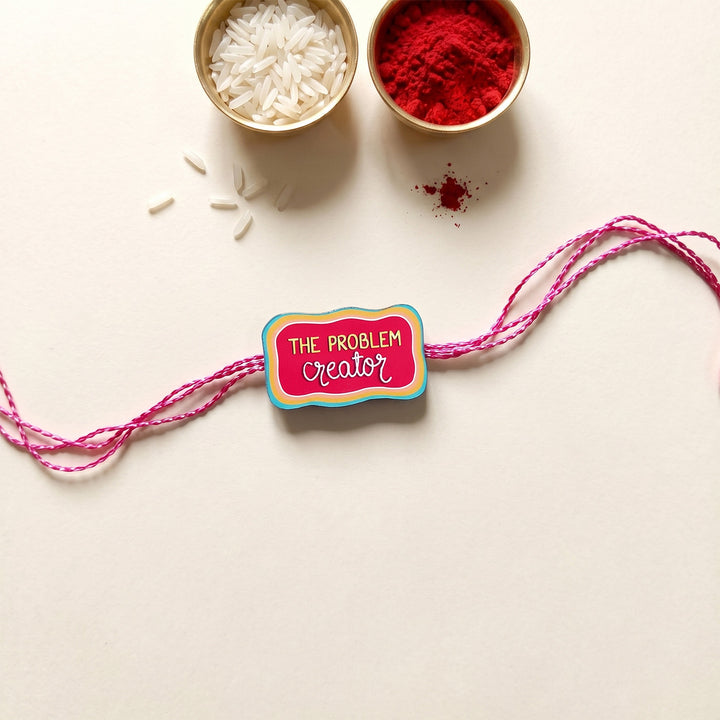 Glossy Printed Wooden 'Problem Creator' Rakhi With Kumkum Rice For Brother