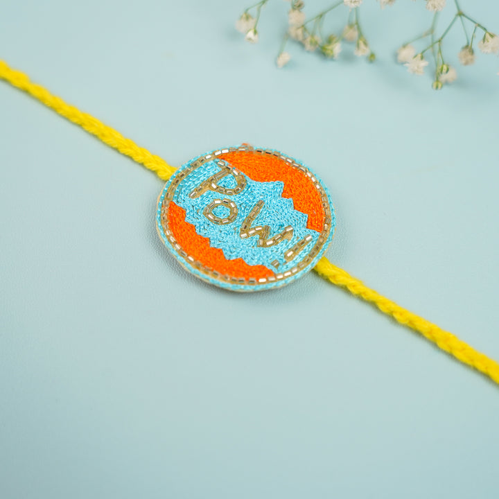 Handmade Beaded Pow Superhero Rakhi With Roli Chawal For Brother - Diagonal Rakhi view with flowers