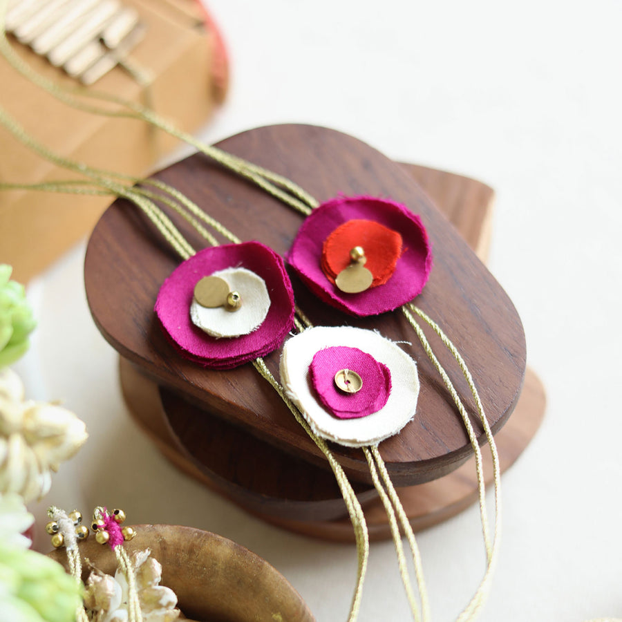 Handmade Reusable Floral And Gold Accent Upcycled Fabric Rakhi With Roli Chawal For Brother Set Of 3 - Necklace on Wooden Stand