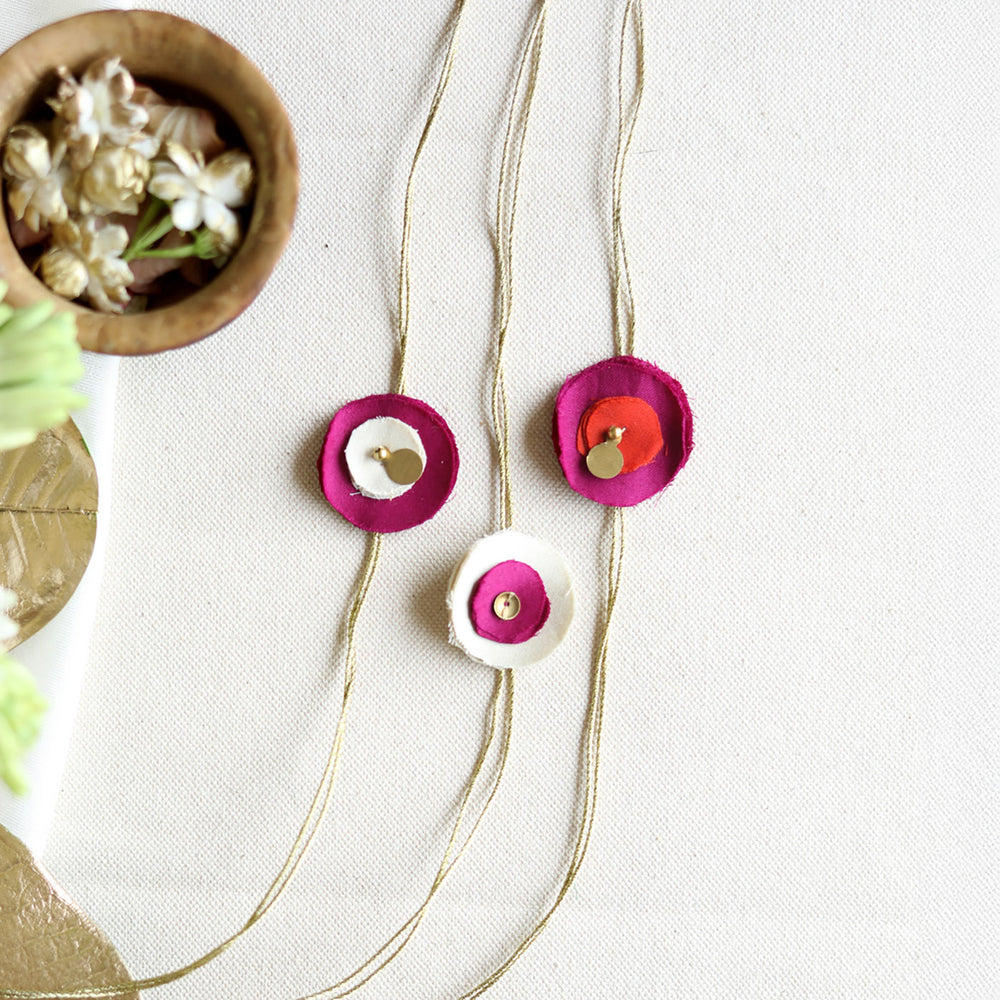 Handmade Reusable Floral And Gold Accent Upcycled Fabric Rakhi With Roli Chawal For Brother Set Of 3 - Flat Lay of Necklace with Charms