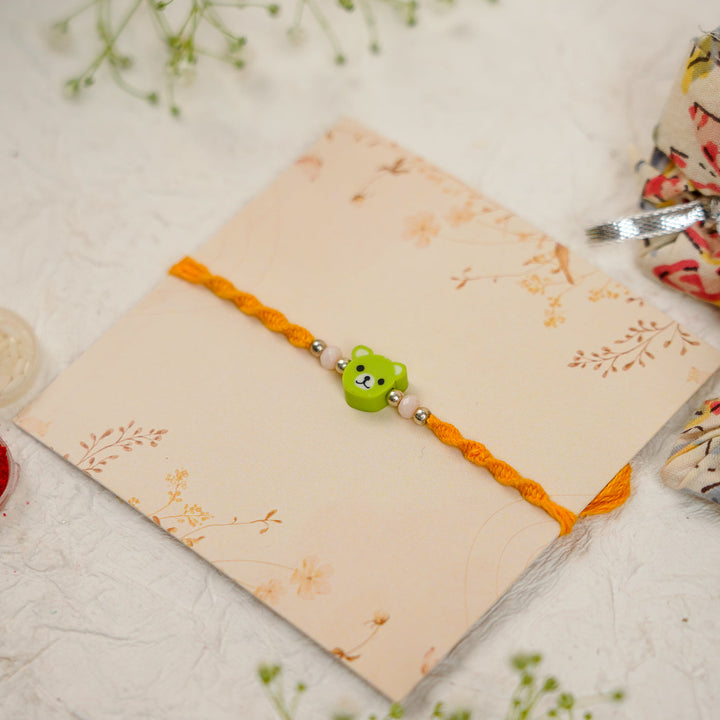 Handmade Green Bear Kids Rakhi With Roli Chawal - Angled View on Decorative Card