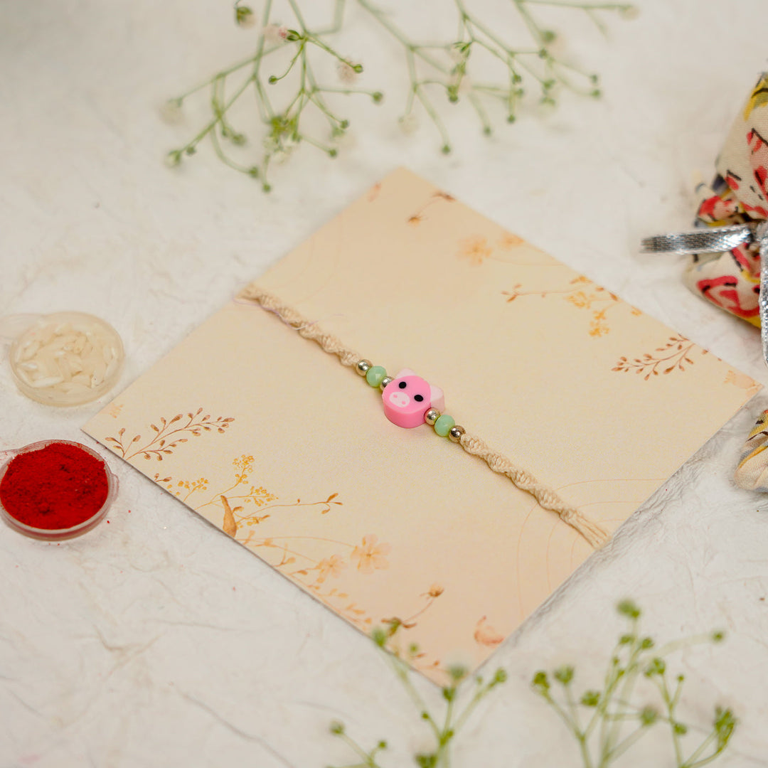 Handmade Pig Kids Rakhi With Roli Chawal - Angled view on presentation card