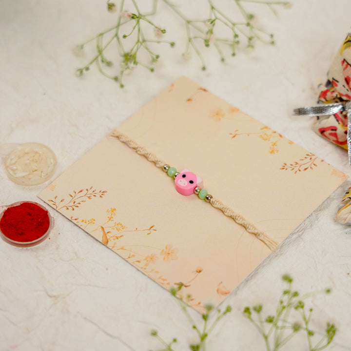 Handmade Pig Kids Rakhi With Roli Chawal - Angled view on presentation card