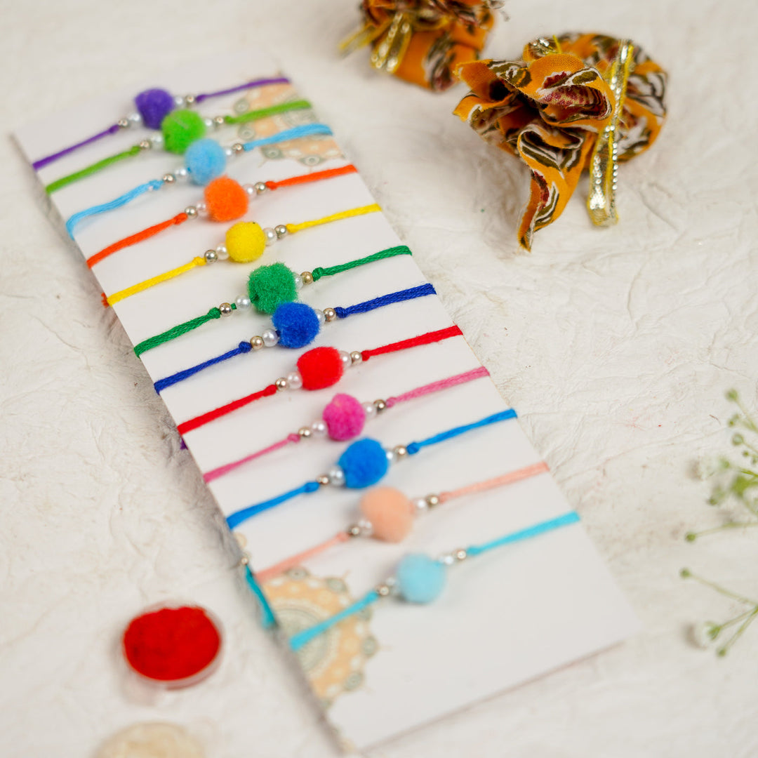 Handmade Small Pompom Rakhi With Roli Chawal Set Of 12 - Angled Top View of Bracelets on Card