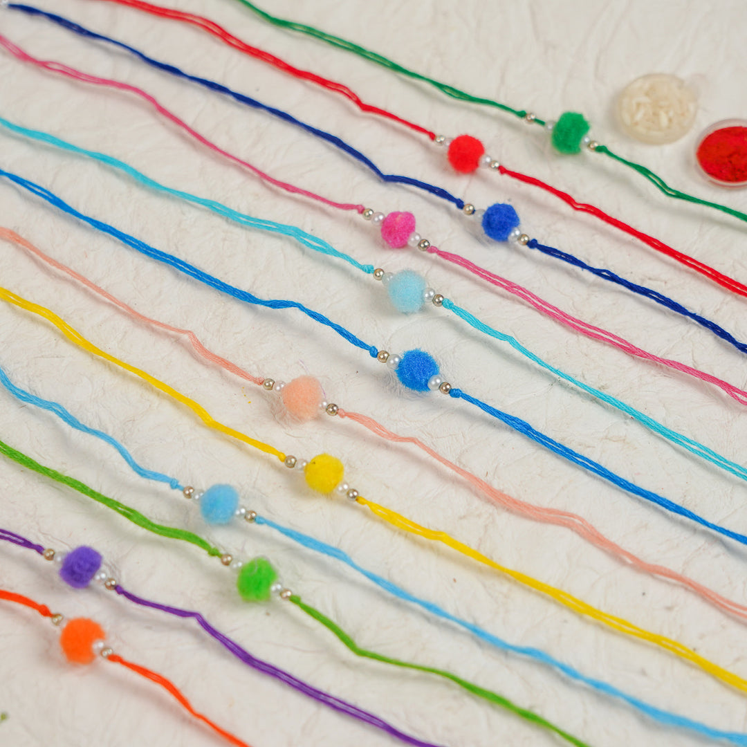Handmade Small Pompom Rakhi With Roli Chawal Set Of 12 - Flat Lay Showing Bracelet Colors