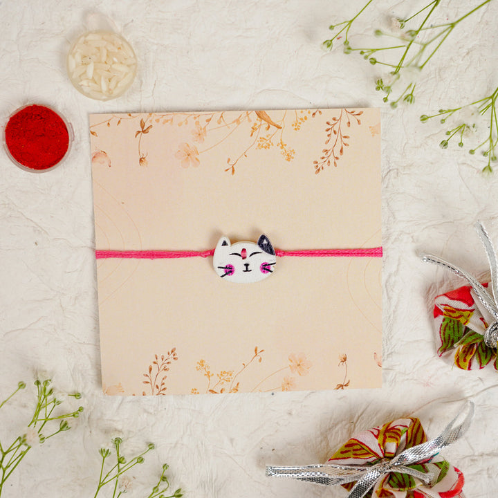 Handmade White Cat Kids Rakhi With Roli Chawal - Flat Lay Front View with Decor