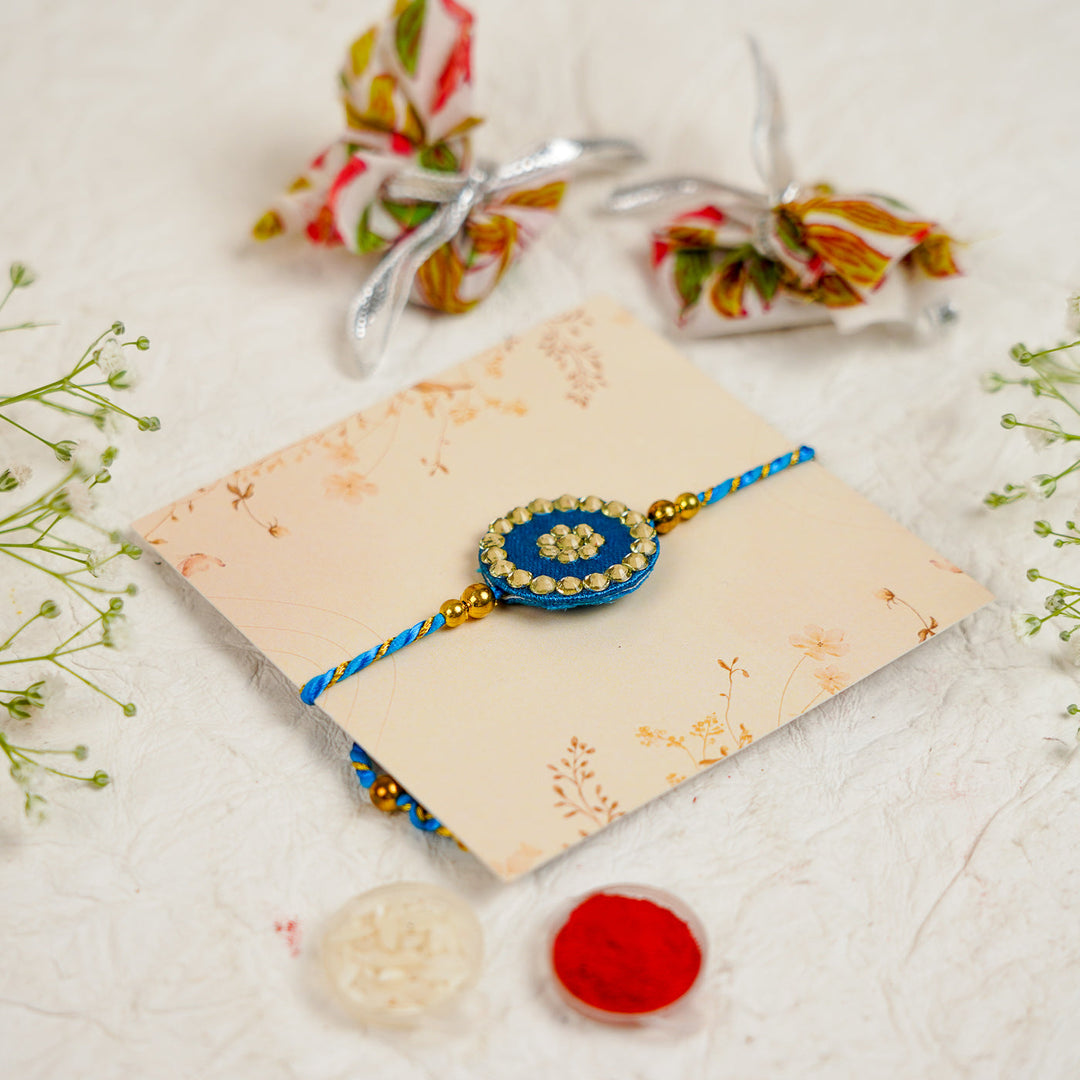 Handmade Silk Crystal Rakhi With Roli Chawal - Angled View Blue Rakhi on Card