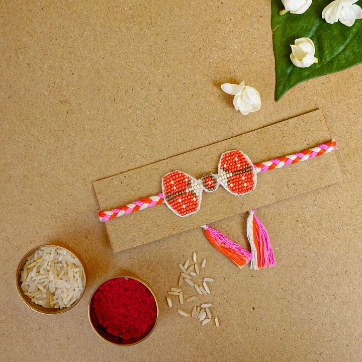 Reusable Beaded Orange Bug Rakhi With Roli Chawal - Flat lay with packaging and accessories