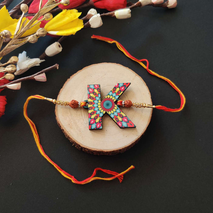 Personalized Handmade Printed Alphabet Wooden Rudraksha Rakhi With Roli Chawal - Flat Lay of Alternate Letter
