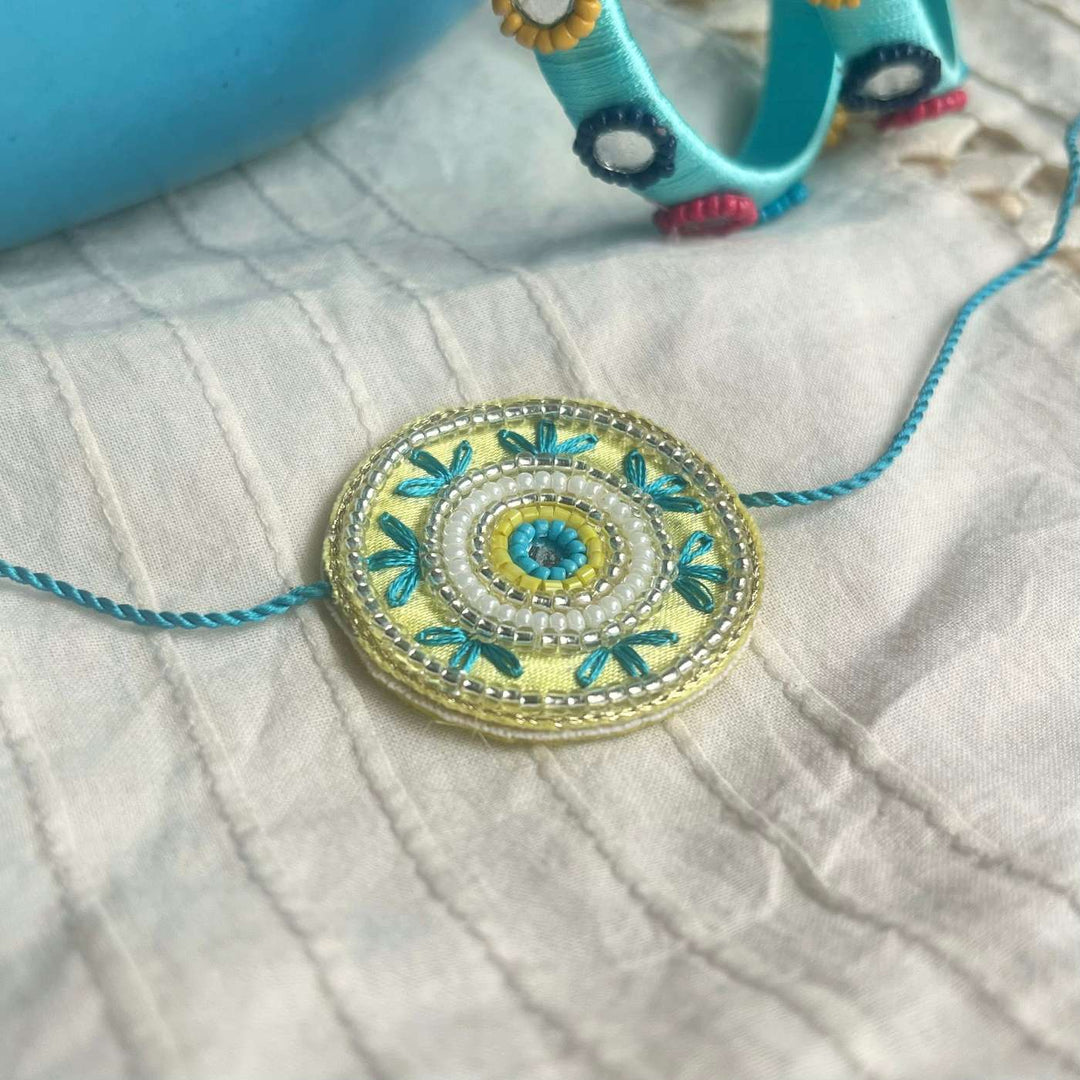 Handmade Beaded Round Rakhi With Roli Chawal - Resting on fabric surface
