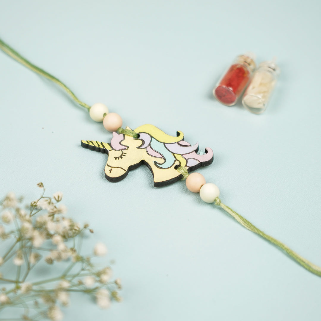 Hand Painted Unicorn Design Mdf Wood Kids Rakhi - Front View with Decorative Items