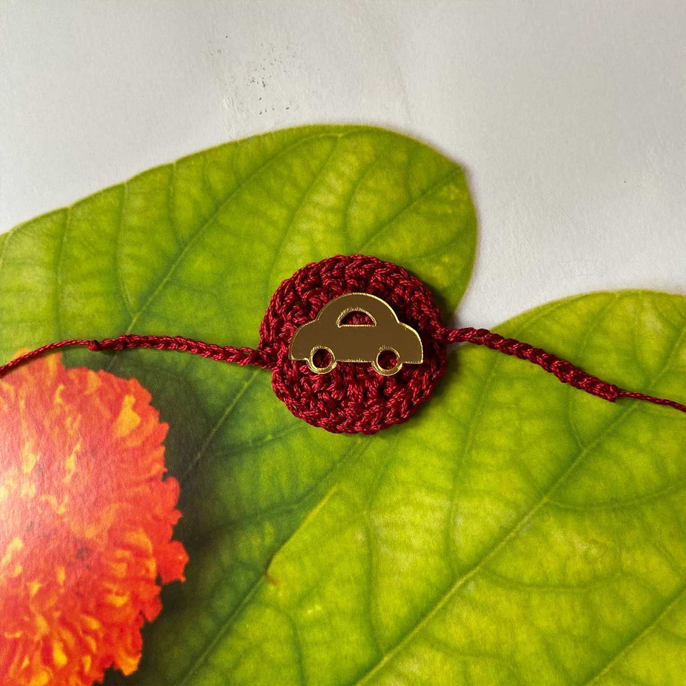 Handmade Crochet Car Theme Cotton Rakhi With Roli Chawal - Full Bracelet Laid on Leaf Background