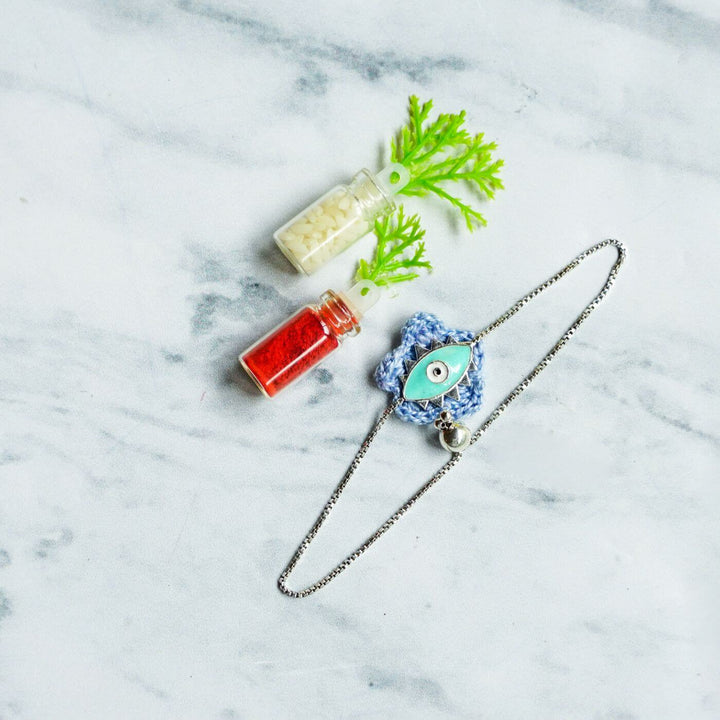 Handcrafted Evil Eye Silver Strap Rakhi For Kids With Rice Roli - Flat Lay with Decorative Bottles