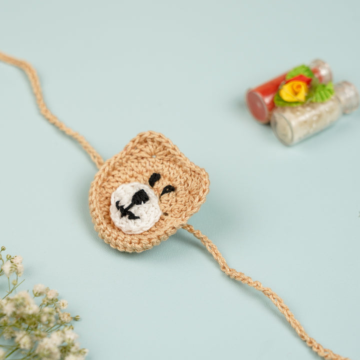 Handmade Crochet Bear Kids Rakhi With Roli Chawal - Front View with Decorative Background