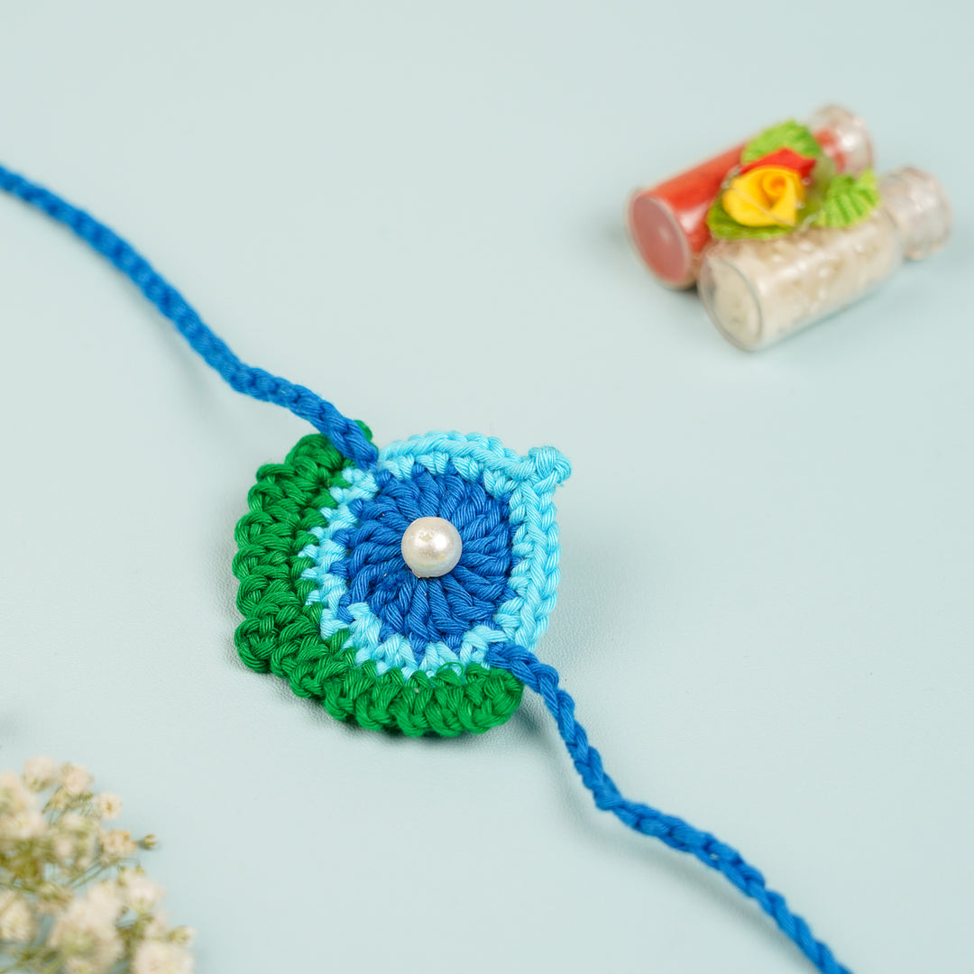 Handmade Crochet Peacock Feather Theme Rakhi With Roli Chawal - Close-up with decorative jars
