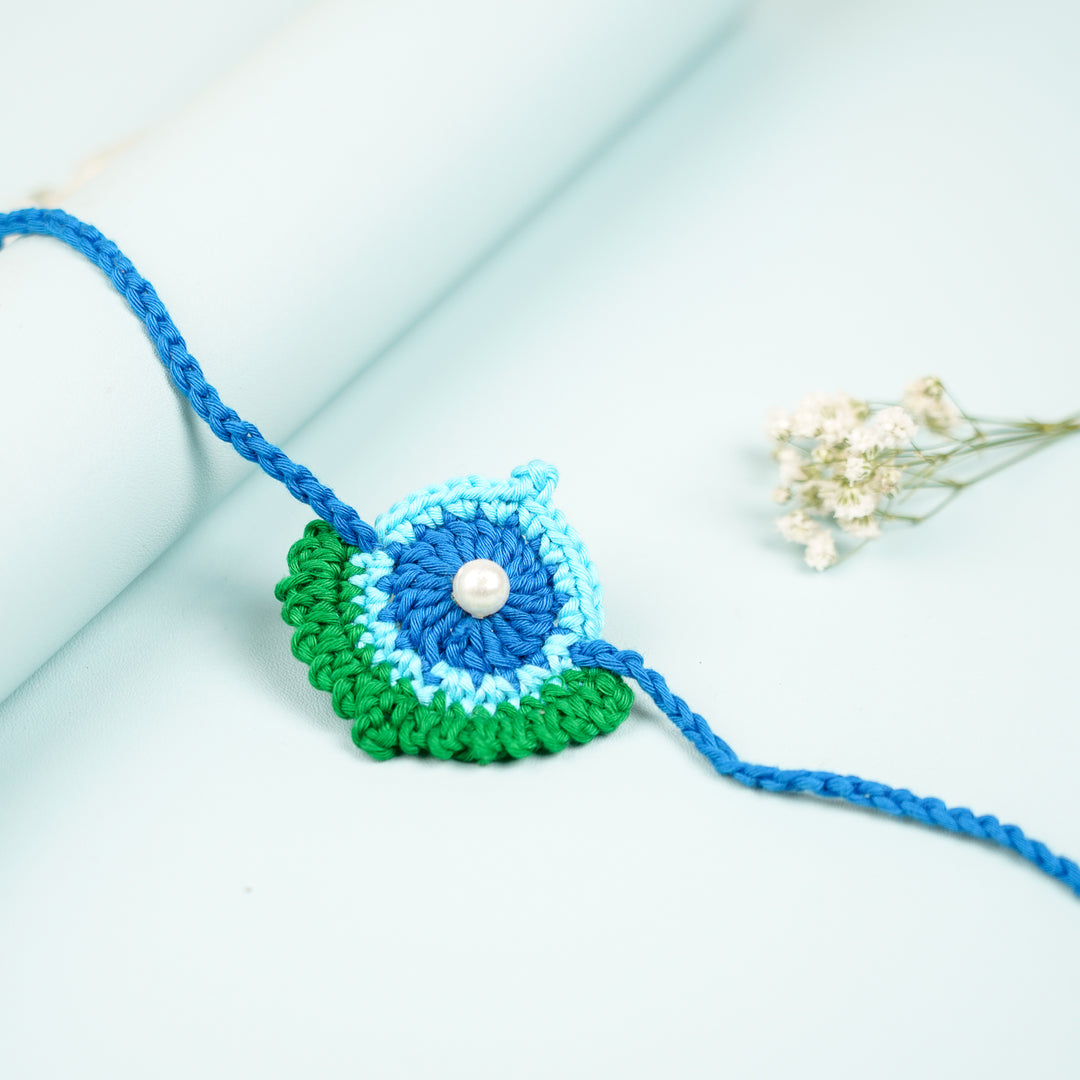 Handmade Crochet Peacock Feather Theme Rakhi With Roli Chawal - Side View with Flower Accent