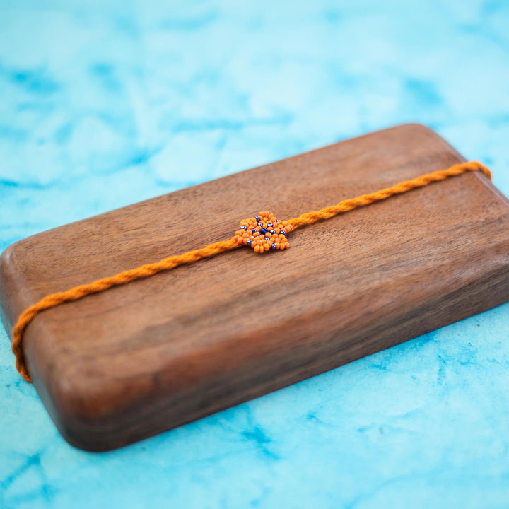 Phool Collection Glass Beeds Rakhi Orange Blue - Diagonal view on wooden surface