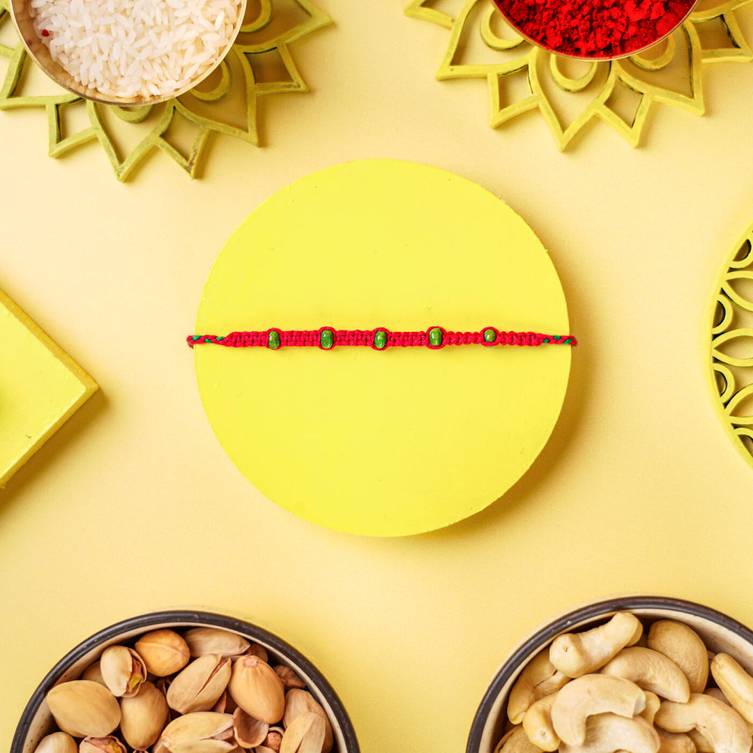 Red Macrame Cotton Rakhi With Green Beads - Flat Lay with Nuts Arrangement