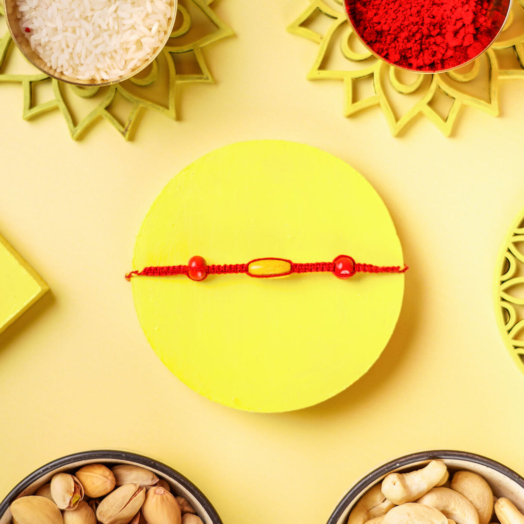 Red Macrame Cotton Rakhi With Red Yellow Beads - Bracelet Flat Lay on Yellow Platform