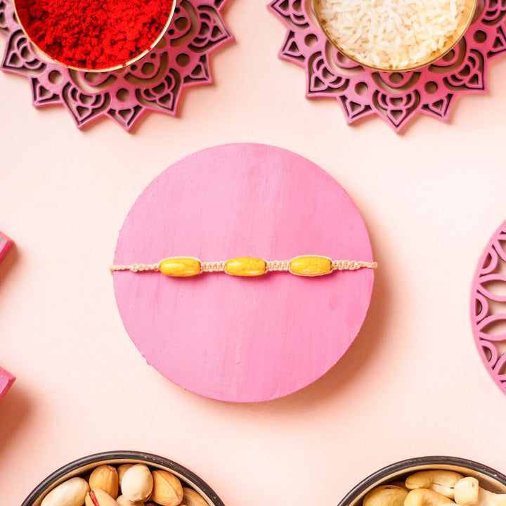 White Macrame Cotton Rakhi With Yellow Beads - Flat lay on pink circle